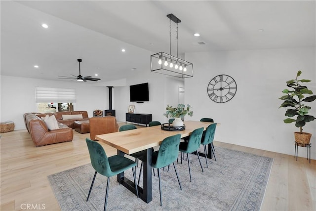 dining area with light wood-type flooring, ceiling fan, and a wood stove