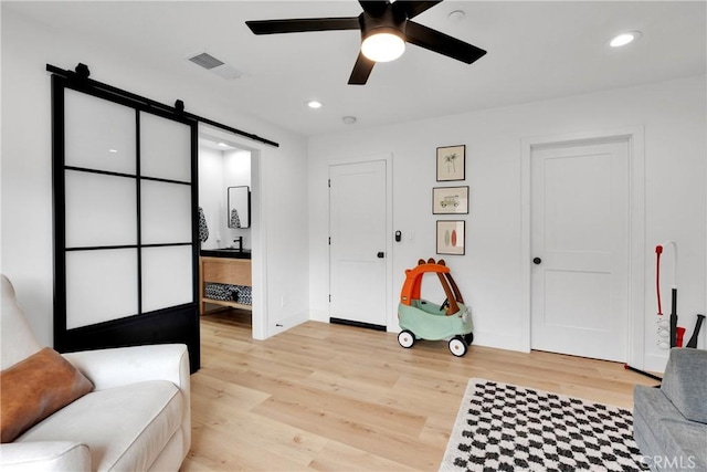 living area featuring a barn door, ceiling fan, and light hardwood / wood-style flooring