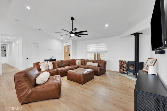 living room with ceiling fan, light hardwood / wood-style flooring, vaulted ceiling, and a wood stove