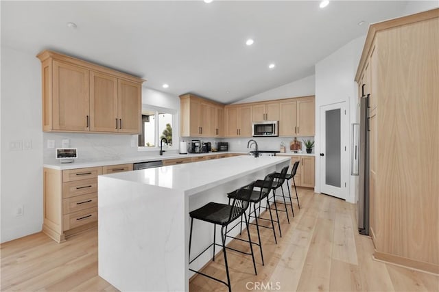 kitchen with stainless steel appliances, a kitchen breakfast bar, light hardwood / wood-style floors, and an island with sink