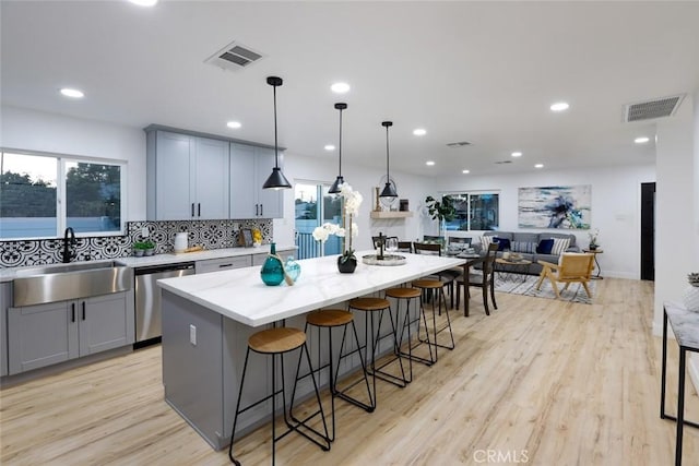 kitchen with a kitchen island, sink, hanging light fixtures, stainless steel dishwasher, and light hardwood / wood-style floors