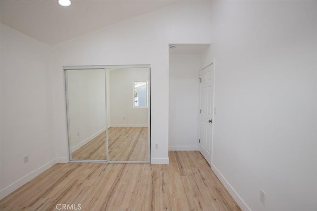 unfurnished bedroom with vaulted ceiling, a closet, and light hardwood / wood-style flooring