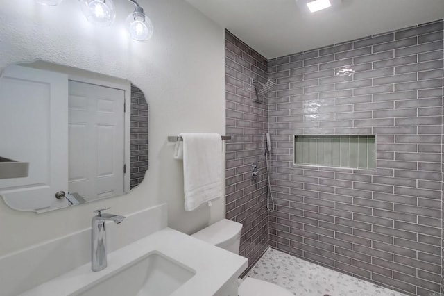 bathroom with tiled shower, vanity, and toilet