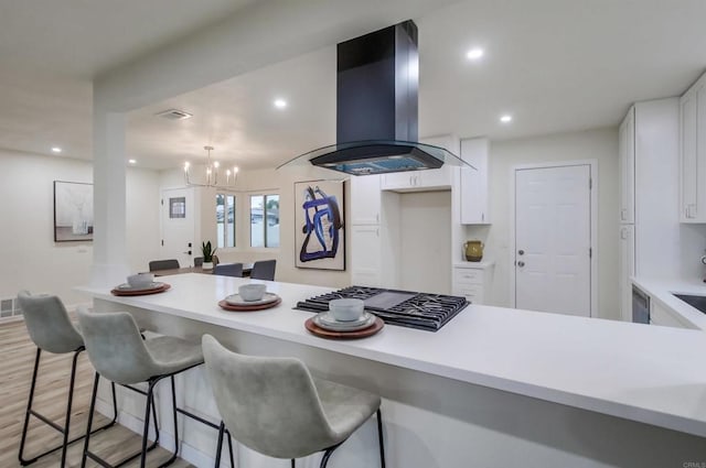 kitchen with island range hood, a breakfast bar area, stainless steel gas cooktop, and white cabinets