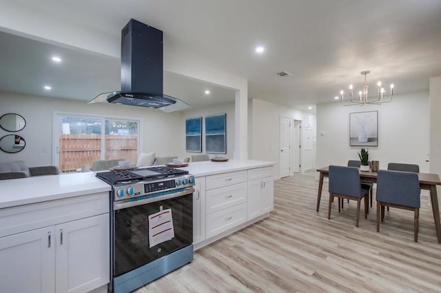 kitchen with gas range, hanging light fixtures, light wood-type flooring, island exhaust hood, and white cabinets