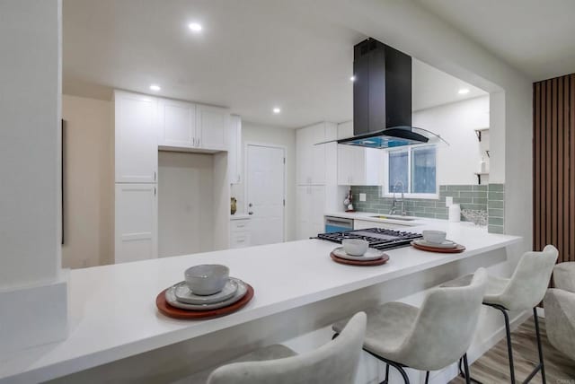 kitchen with stainless steel gas cooktop, a breakfast bar area, white cabinetry, island range hood, and kitchen peninsula