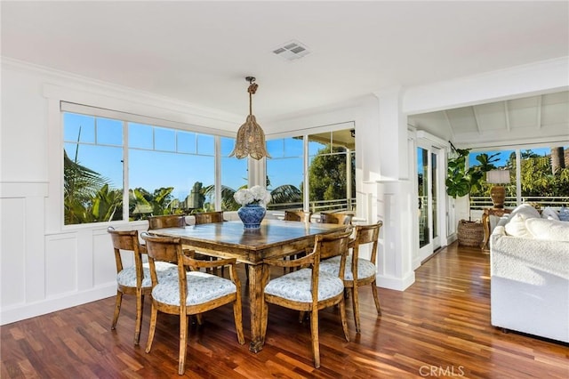 dining area featuring dark wood finished floors, a decorative wall, visible vents, and wainscoting