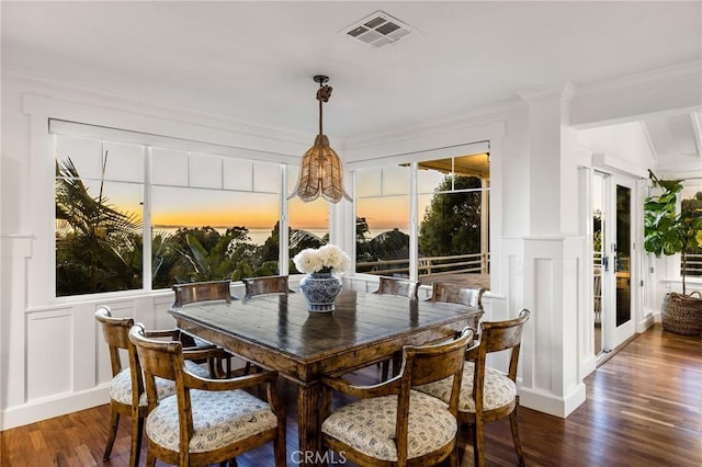 dining area featuring crown molding, a decorative wall, visible vents, wainscoting, and dark wood-style floors
