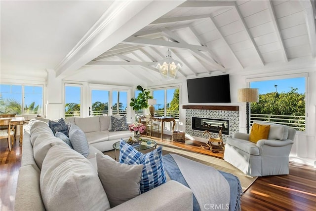 living area with a tiled fireplace, wood finished floors, an inviting chandelier, and lofted ceiling with beams
