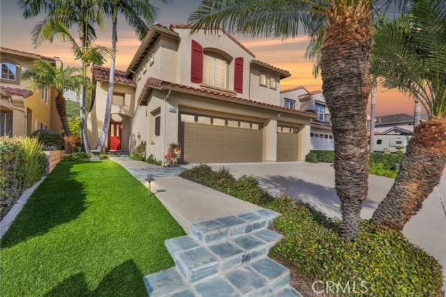 mediterranean / spanish home with a garage, a yard, a tile roof, and stucco siding