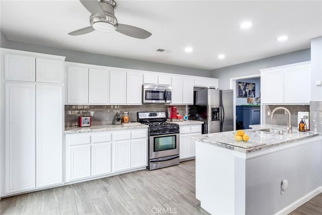 kitchen with sink, white cabinets, kitchen peninsula, stainless steel appliances, and light stone countertops