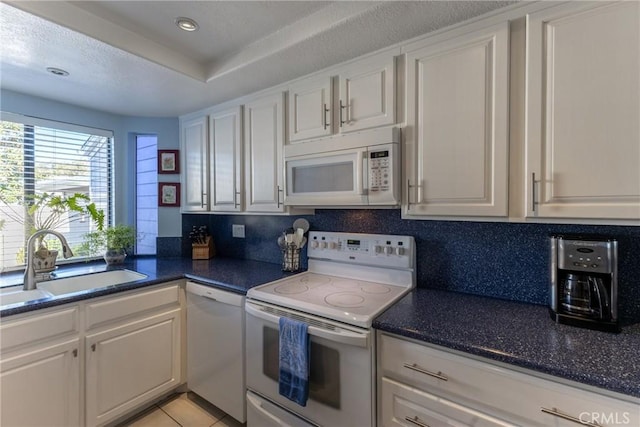 kitchen with white appliances, dark countertops, and white cabinets