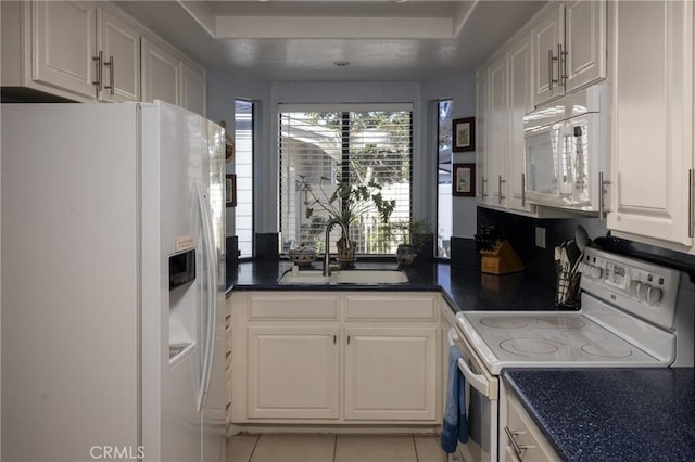 kitchen with dark countertops, white appliances, white cabinetry, and a sink