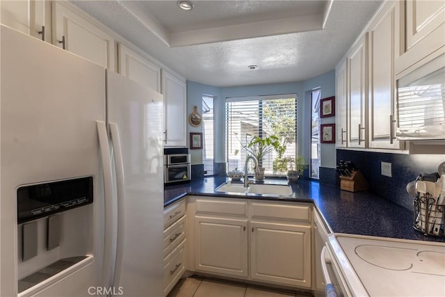 kitchen with a textured ceiling, white fridge with ice dispenser, a sink, and white cabinets