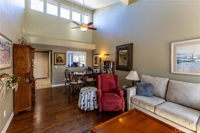 living room featuring ceiling fan, dark wood-type flooring, a towering ceiling, and baseboards