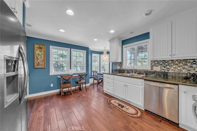 kitchen with a sink, white cabinetry, appliances with stainless steel finishes, decorative backsplash, and dark stone counters