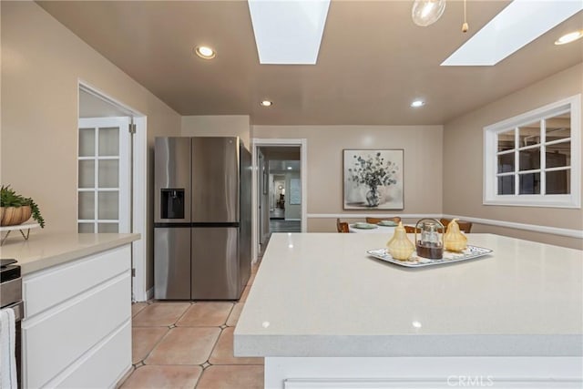 kitchen featuring a kitchen island, a skylight, white cabinets, light tile patterned floors, and stainless steel fridge with ice dispenser