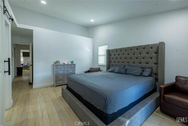 bedroom with a barn door and light wood-type flooring