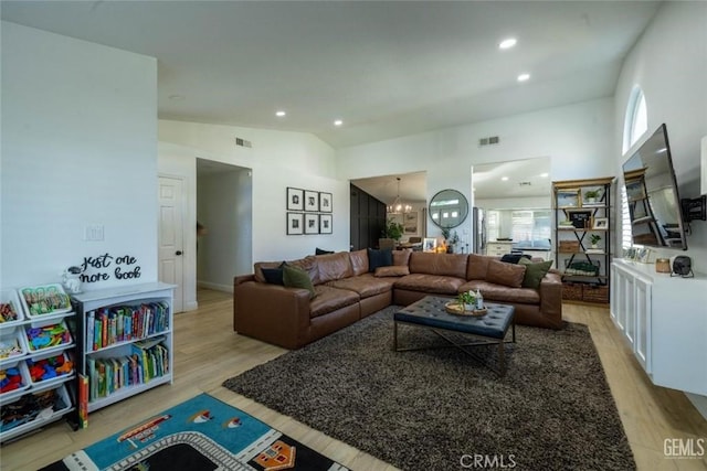 living room featuring high vaulted ceiling, light wood-type flooring, and a chandelier