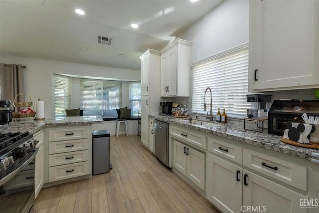 kitchen with appliances with stainless steel finishes, sink, white cabinets, light stone counters, and light wood-type flooring