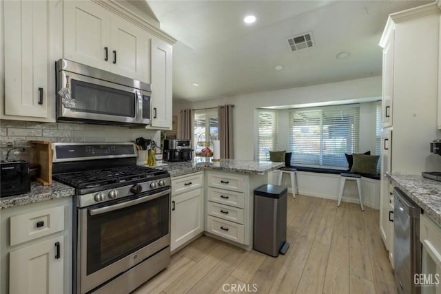 kitchen featuring appliances with stainless steel finishes, white cabinetry, kitchen peninsula, light stone countertops, and light wood-type flooring