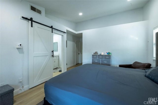 bedroom with ensuite bathroom, a barn door, and light hardwood / wood-style floors