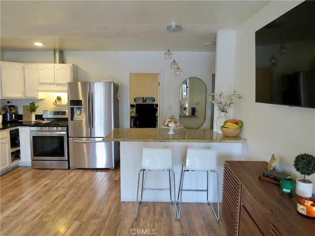 kitchen with appliances with stainless steel finishes, a kitchen breakfast bar, kitchen peninsula, light stone countertops, and white cabinets