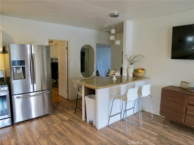 kitchen with stainless steel appliances, kitchen peninsula, a breakfast bar area, and light hardwood / wood-style flooring