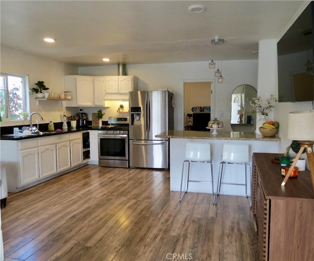 kitchen featuring white cabinetry, appliances with stainless steel finishes, hardwood / wood-style floors, and dark stone countertops