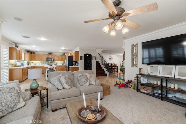 living room with visible vents, ceiling fan, stairs, crown molding, and light colored carpet