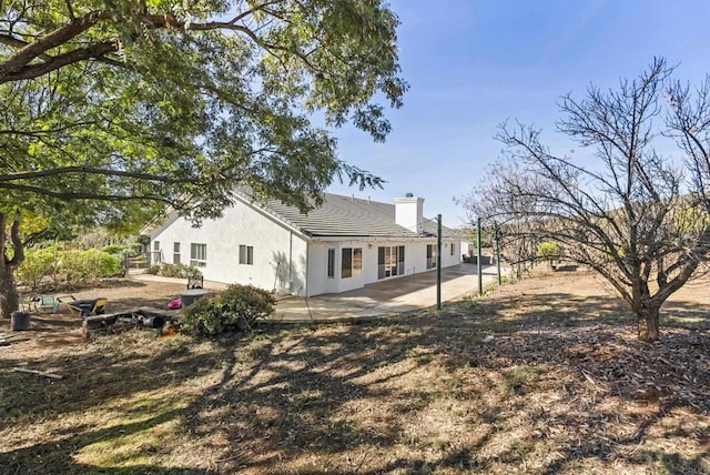 back of house with a chimney, a patio area, and stucco siding