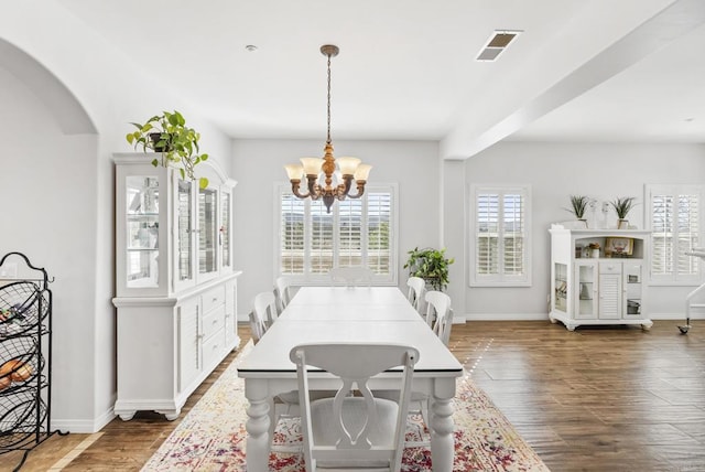 dining area featuring dark wood-style flooring, visible vents, a notable chandelier, and baseboards