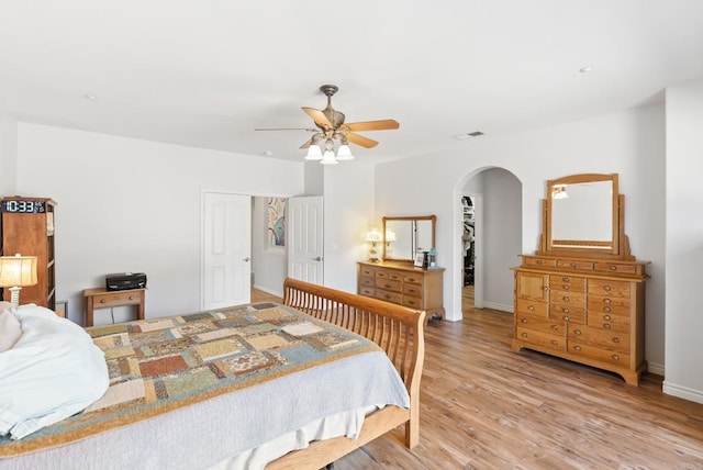 bedroom featuring visible vents, arched walkways, baseboards, light wood-style flooring, and ceiling fan