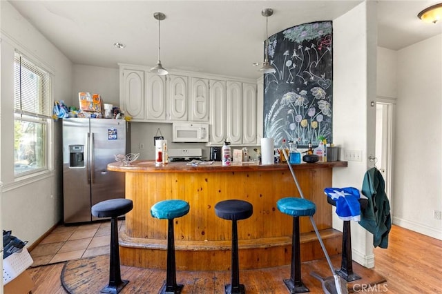 kitchen featuring a breakfast bar area, hanging light fixtures, white cabinets, stainless steel fridge with ice dispenser, and kitchen peninsula