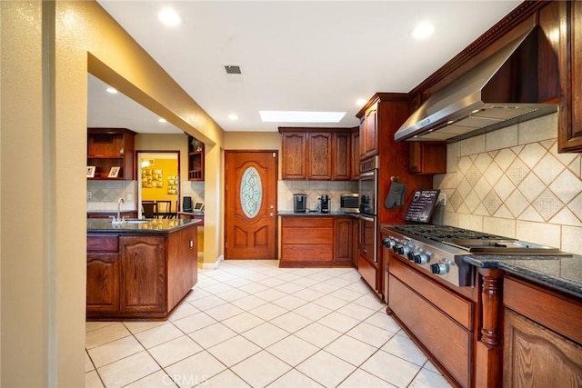 kitchen with appliances with stainless steel finishes, sink, dark stone countertops, light tile patterned floors, and wall chimney range hood