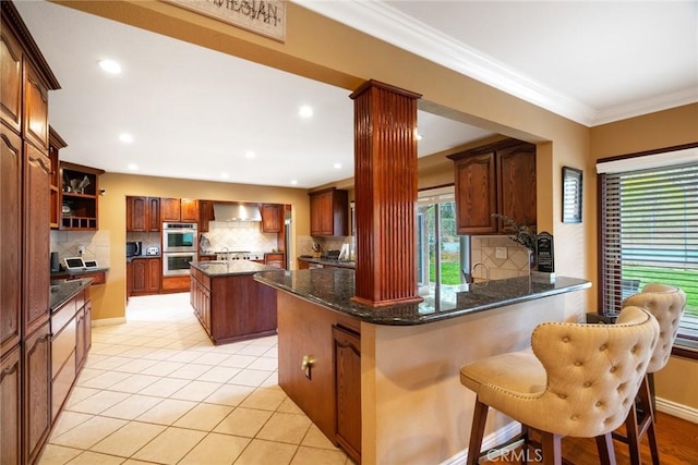 kitchen featuring a center island, light tile patterned floors, a kitchen breakfast bar, kitchen peninsula, and wall chimney range hood