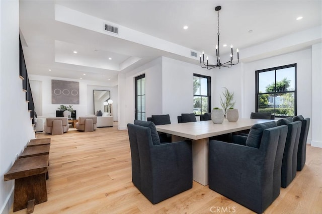 dining space with an inviting chandelier, a tray ceiling, and light hardwood / wood-style flooring