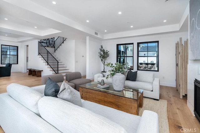 living room with a raised ceiling, a high end fireplace, and light hardwood / wood-style floors