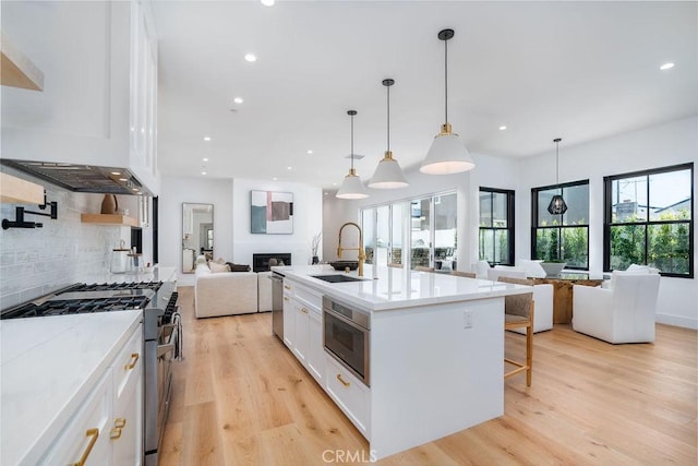 kitchen featuring white cabinetry, an island with sink, sink, hanging light fixtures, and stainless steel appliances