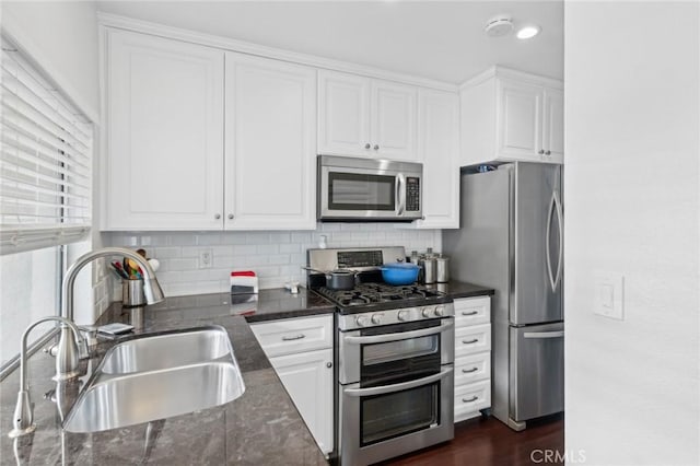 kitchen with sink, white cabinetry, appliances with stainless steel finishes, dark stone counters, and backsplash