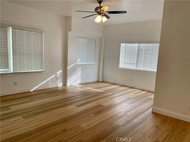 spare room featuring light wood finished floors, a ceiling fan, and baseboards