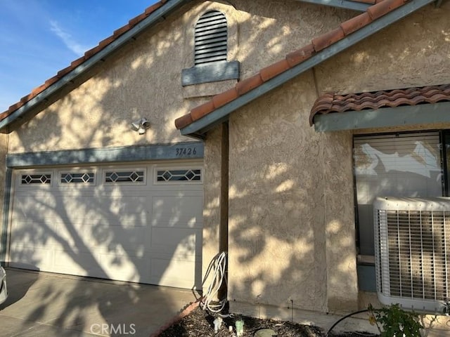 view of side of property with a tile roof, central AC unit, a garage, and stucco siding