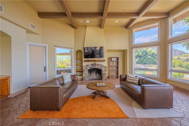 living room featuring a towering ceiling, a stone fireplace, and beamed ceiling