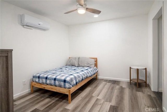 bedroom with wood-type flooring, a wall mounted air conditioner, and ceiling fan