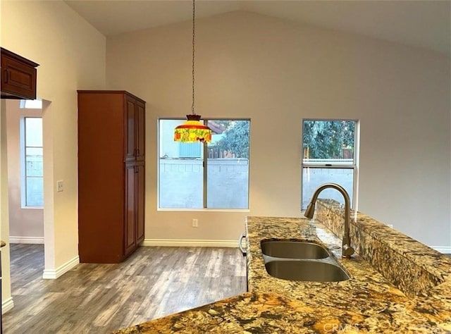 kitchen with sink, hardwood / wood-style flooring, high vaulted ceiling, light stone countertops, and decorative light fixtures