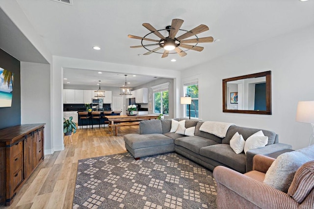 living room featuring ceiling fan with notable chandelier and light hardwood / wood-style flooring