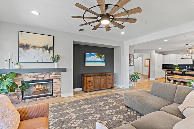 living room with sink, ceiling fan with notable chandelier, a fireplace, and light hardwood / wood-style floors