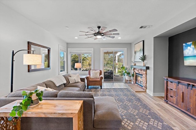 living room with a stone fireplace, ceiling fan, and light hardwood / wood-style flooring