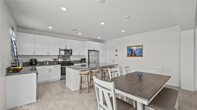 kitchen featuring a breakfast bar area, white cabinetry, a center island, dark stone counters, and stainless steel appliances