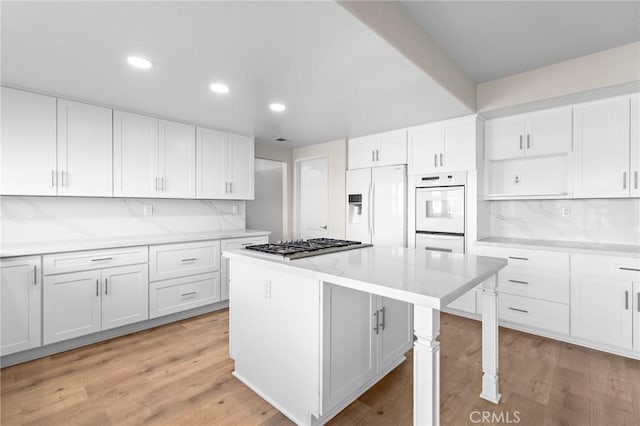 kitchen featuring light wood-style flooring, white appliances, a kitchen island, and white cabinetry